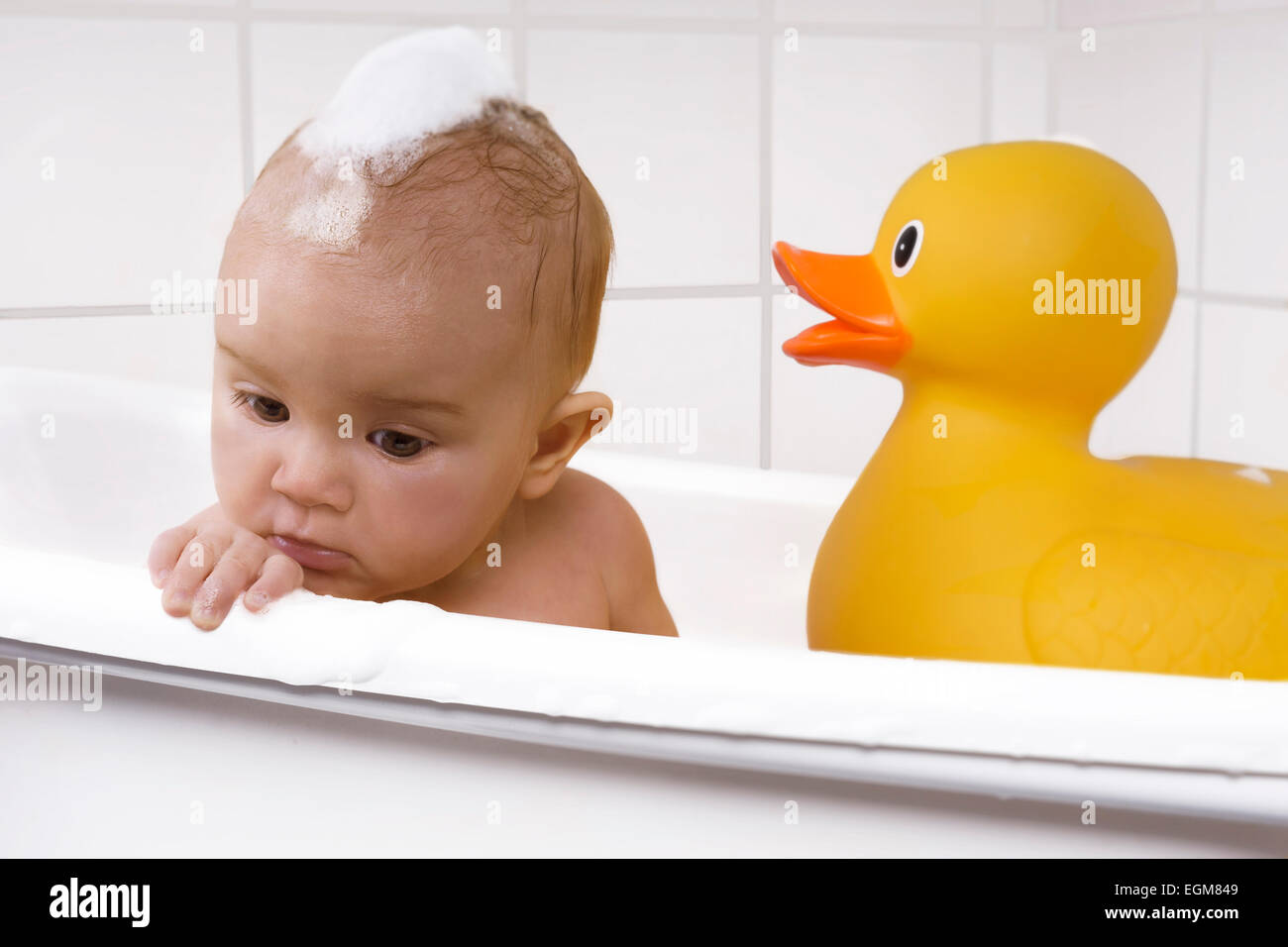 Carino baby ragazza seduta in una vasca con un anatra di gomma Foto Stock