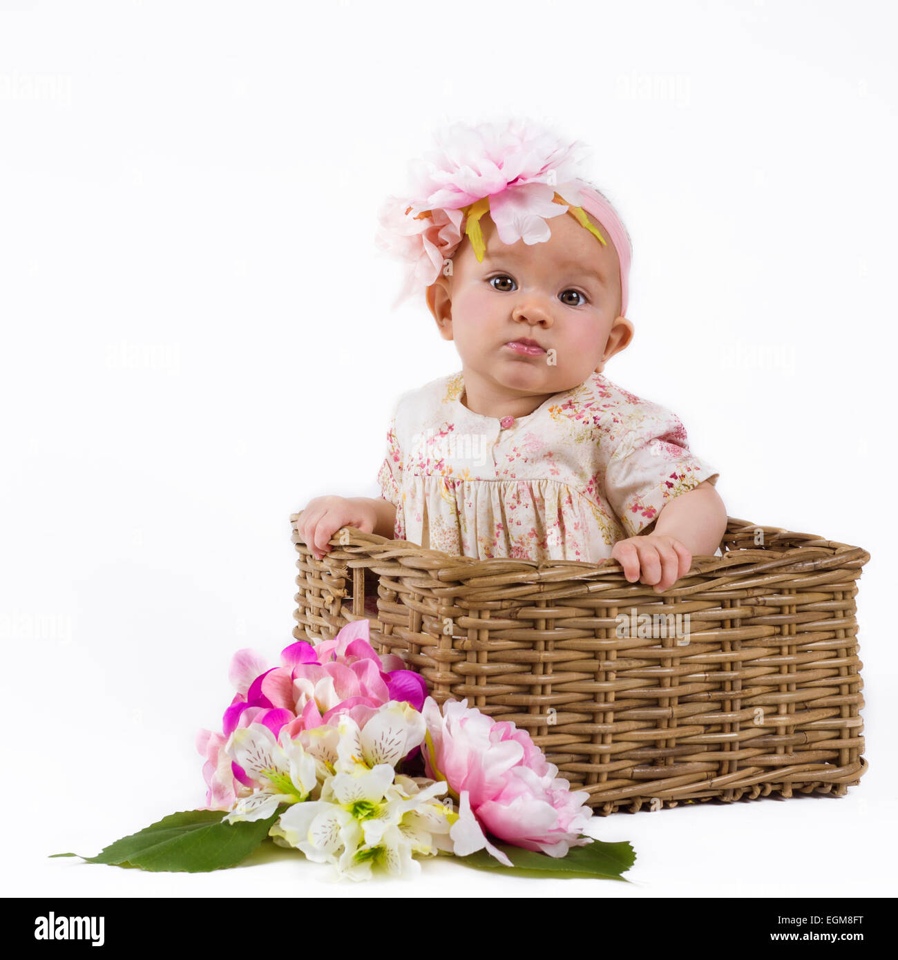 Carino il neonato in un abito di fiori seduti in un cesto fiorito Foto Stock