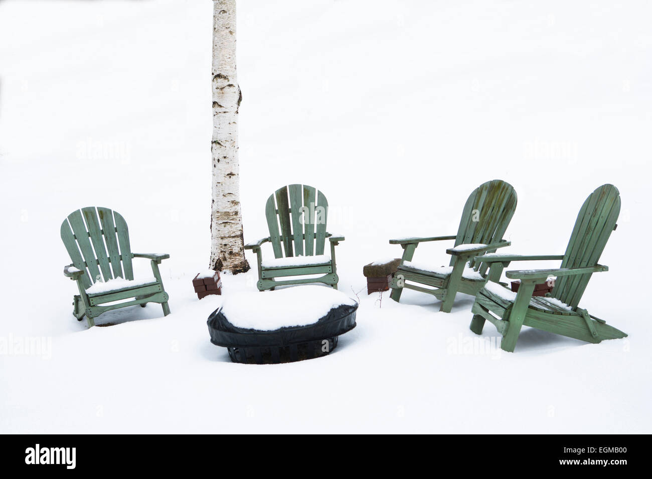 Una buca per il fuoco e sedie Adirondack nella neve nei pressi di betulla Foto Stock