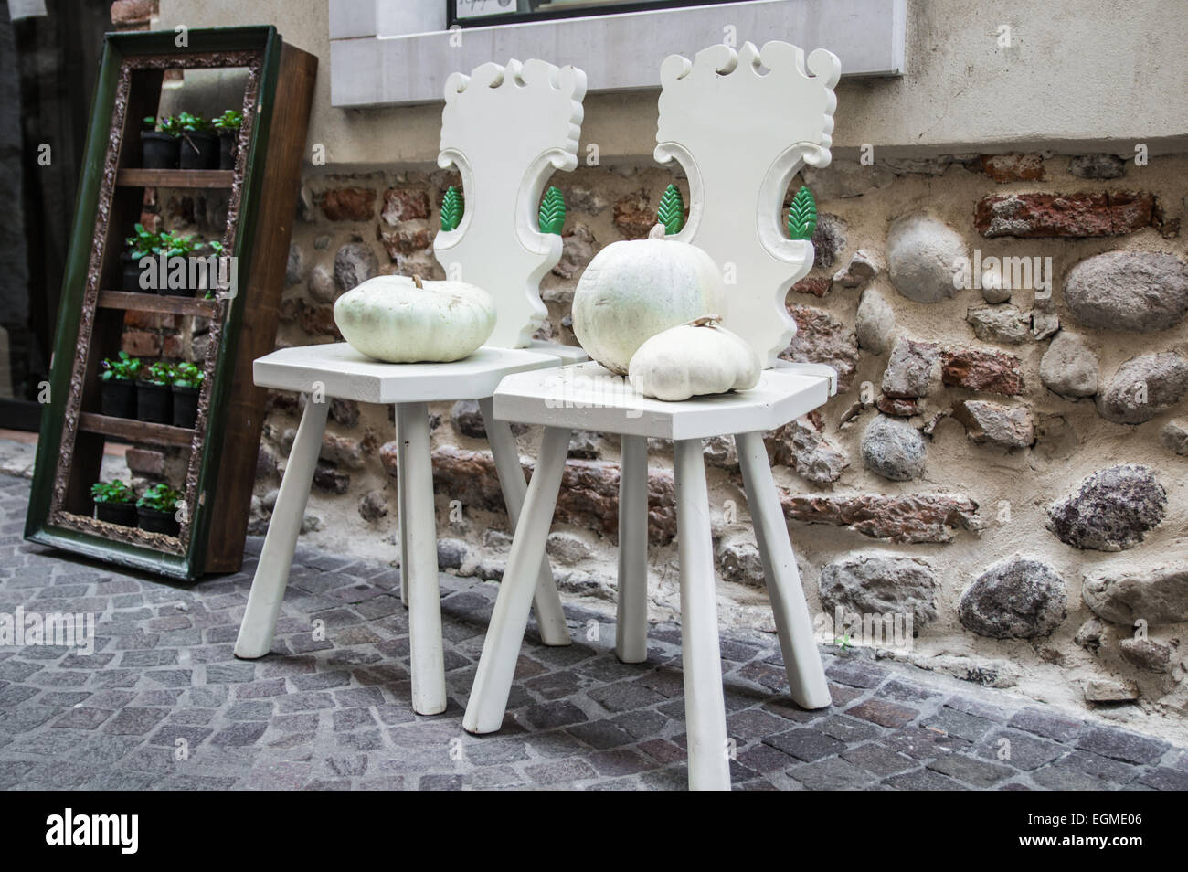 Due sedie in legno dipinto di bianco e due zucche bianco contro la parete lungo una strada Foto Stock