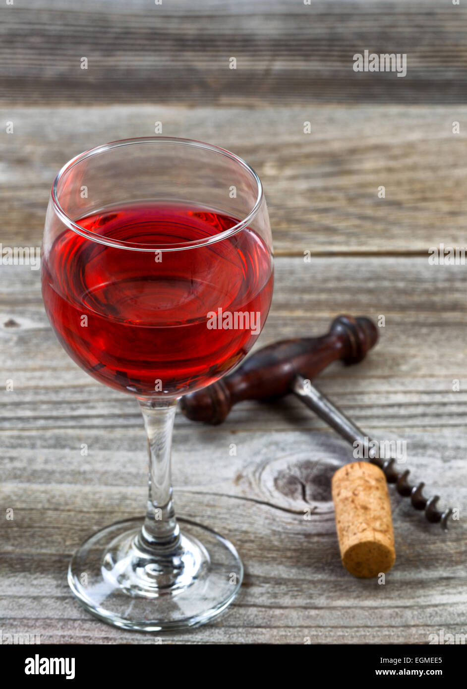 L'immagine verticale di vino rosso, focus sul labbro anteriore del vetro, con antichi cavatappi e sughero in background su legno rustico. Foto Stock