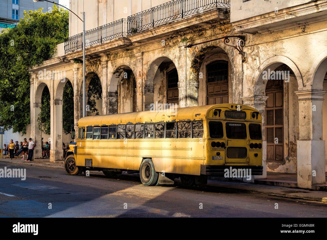 Un classico anni cinquanta Americana scuola giallo autobus parcheggiato sul lato della strada a l'Avana, Cuba, accanto all architettura coloniale. Foto Stock