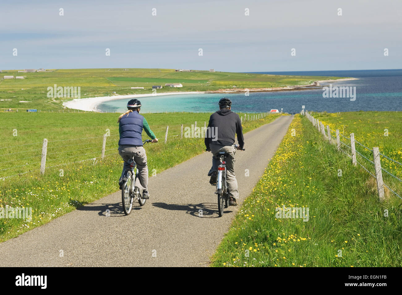 Giovane uomo e donna in bicicletta lungo una strada tranquilla in Deerness, Orkney Islands, Scozia. Foto Stock