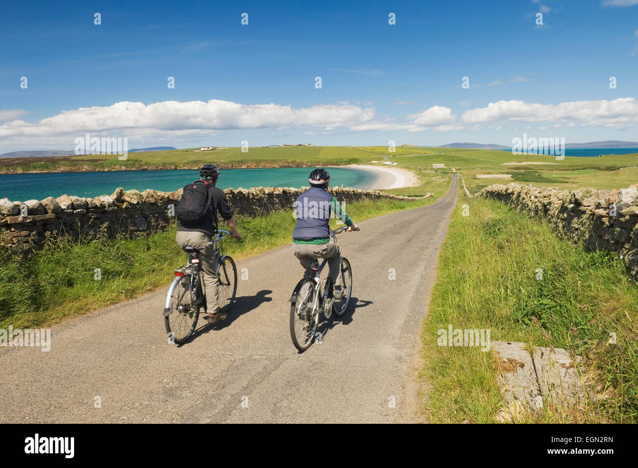 Giovane uomo e donna in bicicletta lungo una tranquilla strada sul South Ronaldsay, Orkney Islands, Scozia. Foto Stock