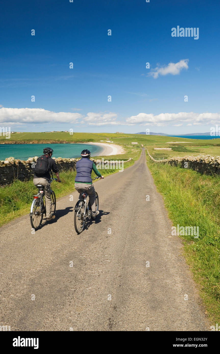 Giovane uomo e donna in bicicletta lungo una tranquilla strada sul South Ronaldsay, Orkney Islands, Scozia. Foto Stock