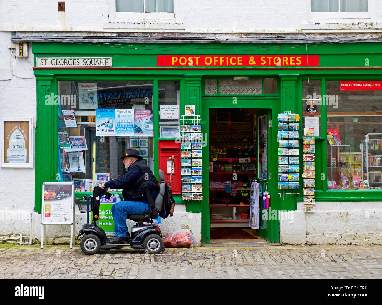 Senior uomo su scooter di mobilità al di fuori del villaggio post office, Mevagissey, Cornwall, England Regno Unito Foto Stock