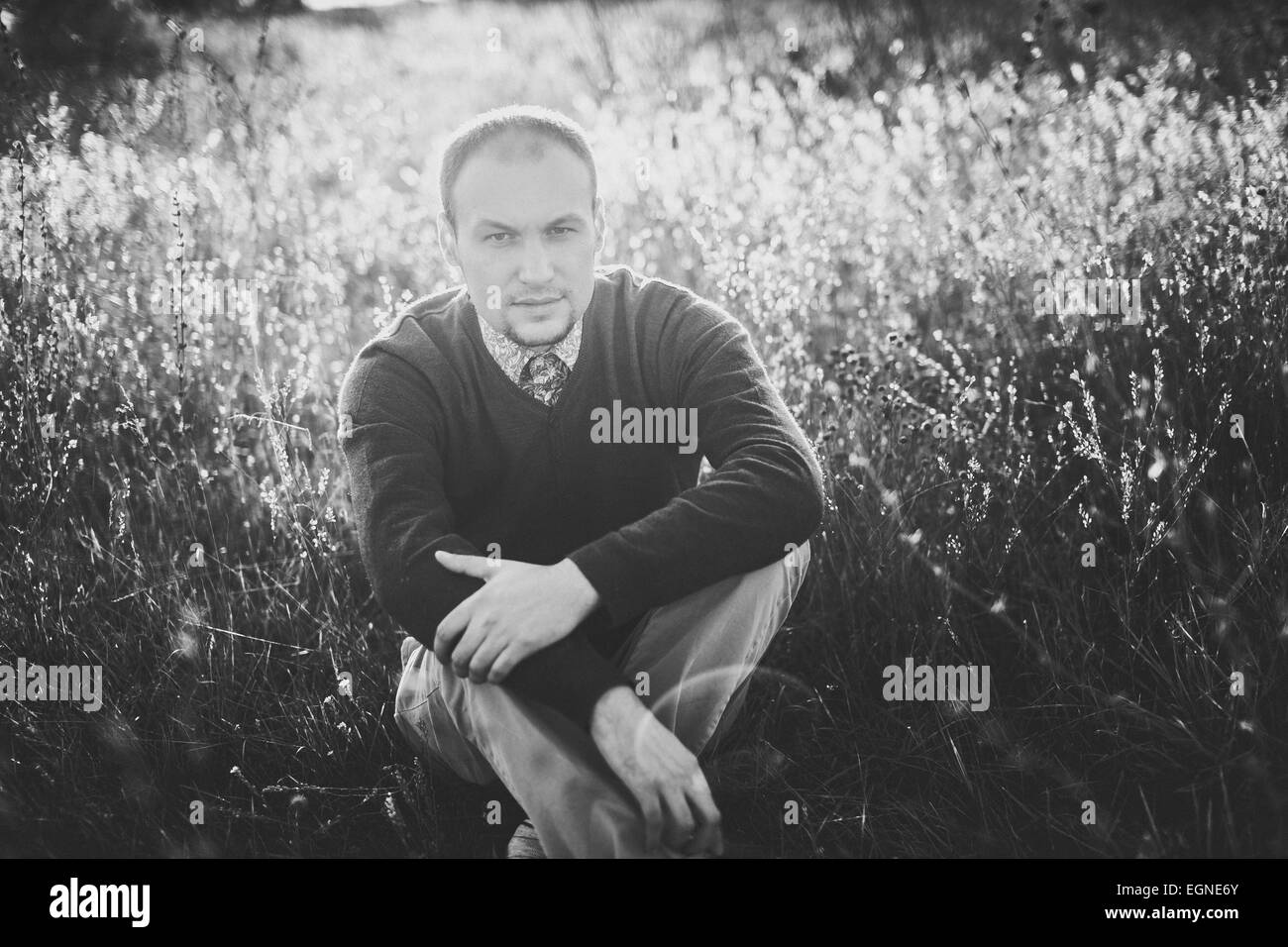Immagine in bianco e nero di un giovane uomo sittin sull'erba al tramonto Foto Stock