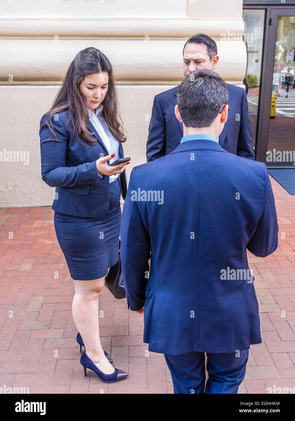 Tre persone d'affari, due uomini e una donna, tutti vestiti .in tute blu, in piedi insieme su un marciapiede sulla strada dello Stato controllo Foto Stock