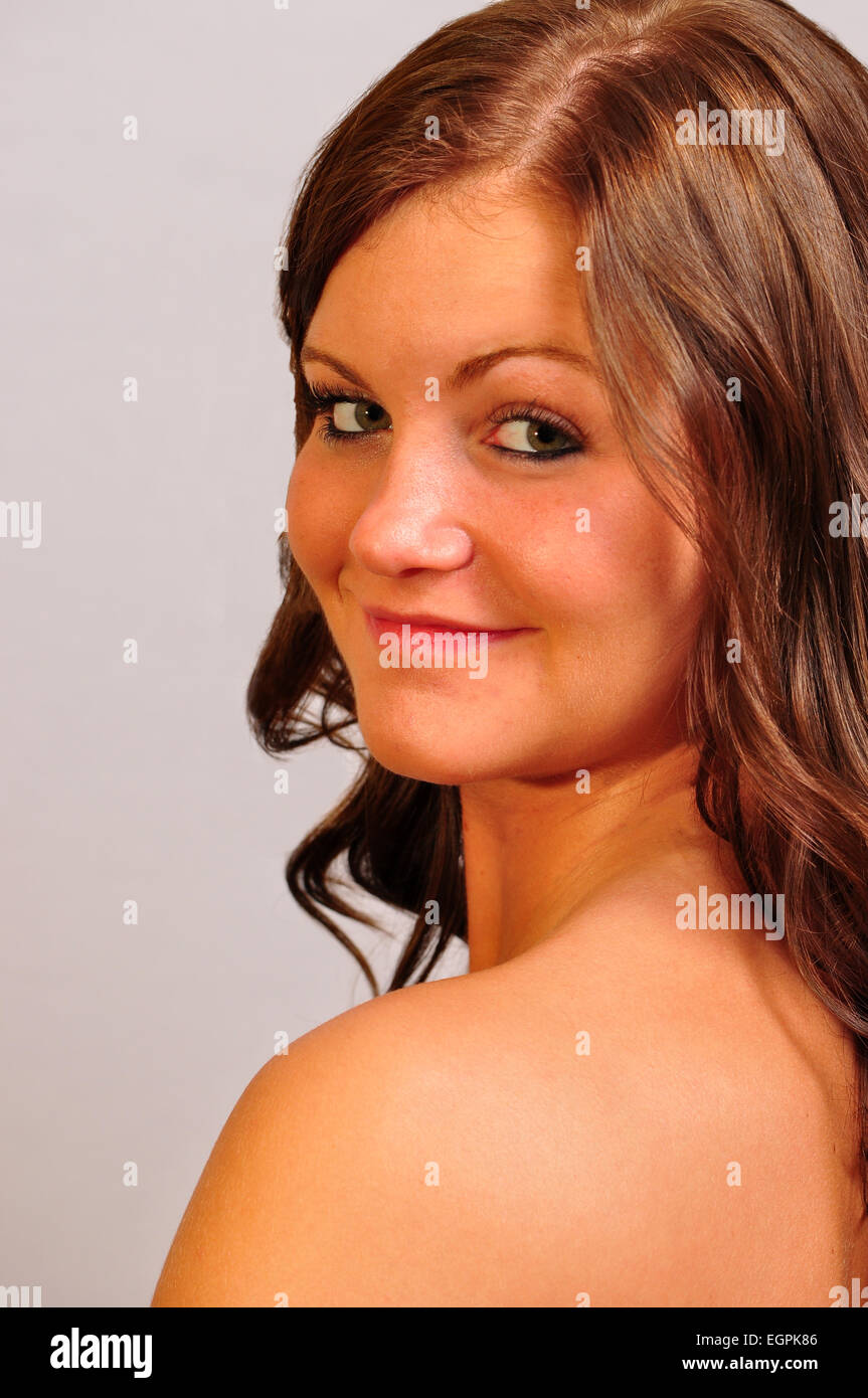 Un attraente giovane donna guardando sopra la sua spalla cercando nella fotocamera. Foto Stock