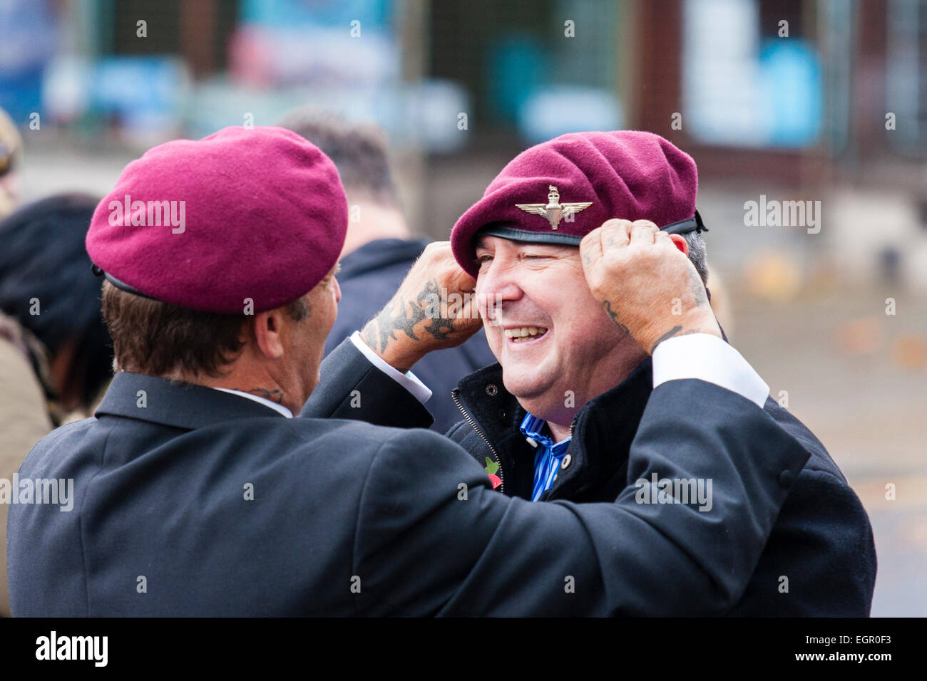 Due uomini maturi, vestiti di giacche e paracadutisti beret, in piedi fuori chiacchierando ad un evento militare. Uno sta regolando il beret dell'altro. Foto Stock