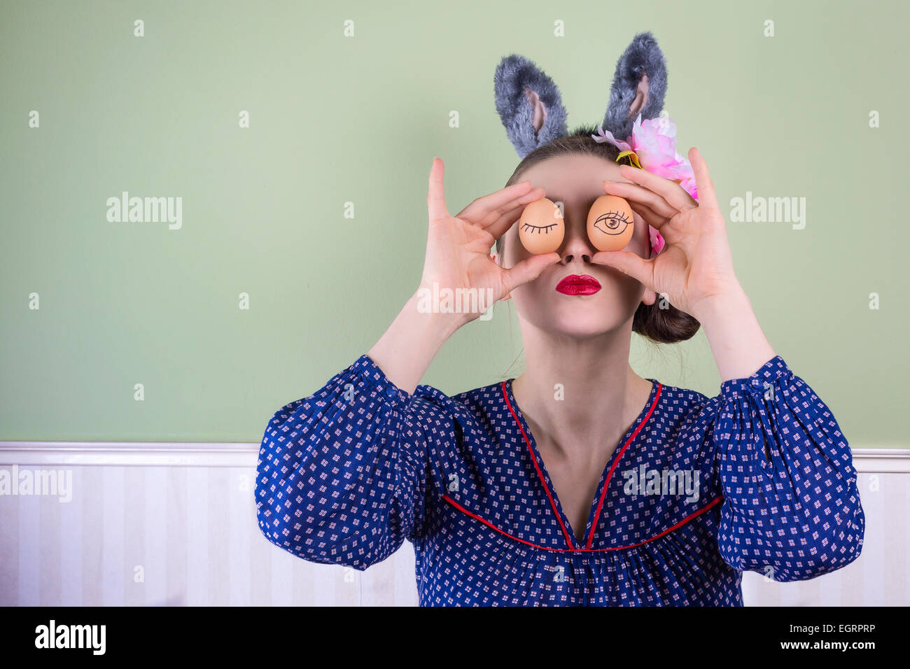 Ritratto di una giovane donna che indossa orecchie di coniglietto tenendo due uova davanti agli occhi. Foto Stock