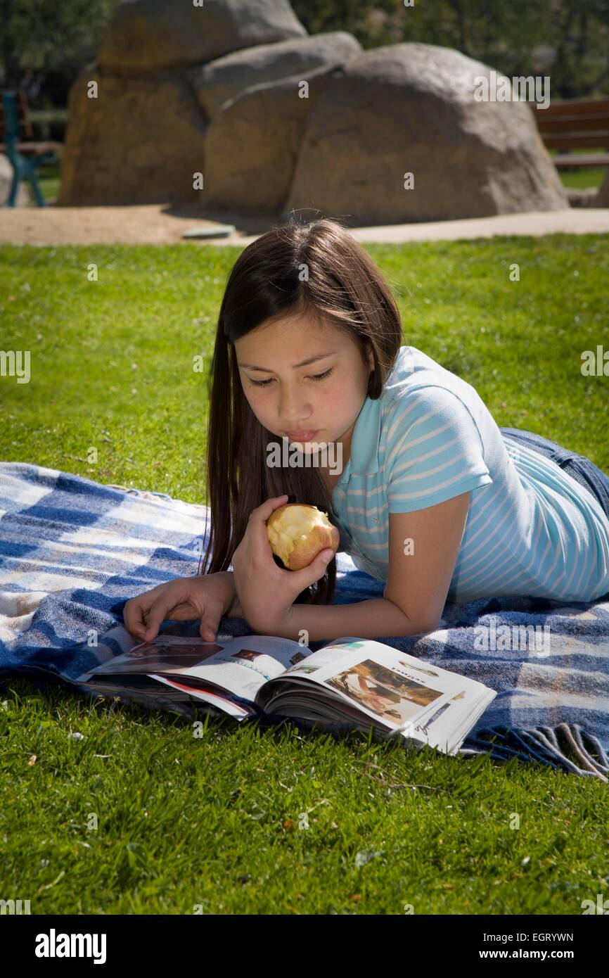 12 -13 anni di razza mista vietnamita caucasica/lettura della ragazza rivista sul parco di erba giovane gente Tween tween signor © Myrleen Pearson Foto Stock