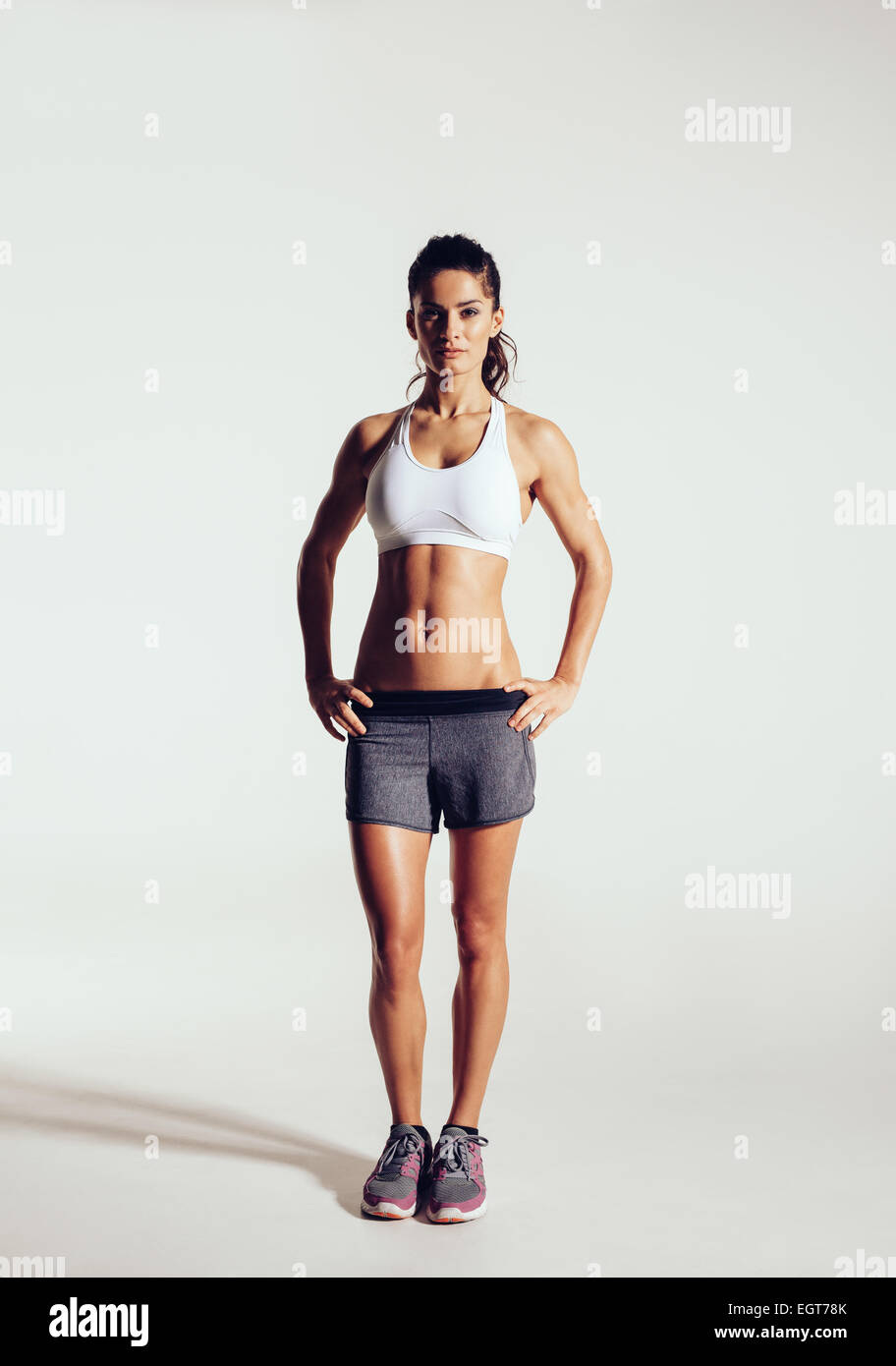Giovane donna con bella slim corpo sano in posa di studio. Fitness modello femminile in sportswear su sfondo grigio Foto Stock
