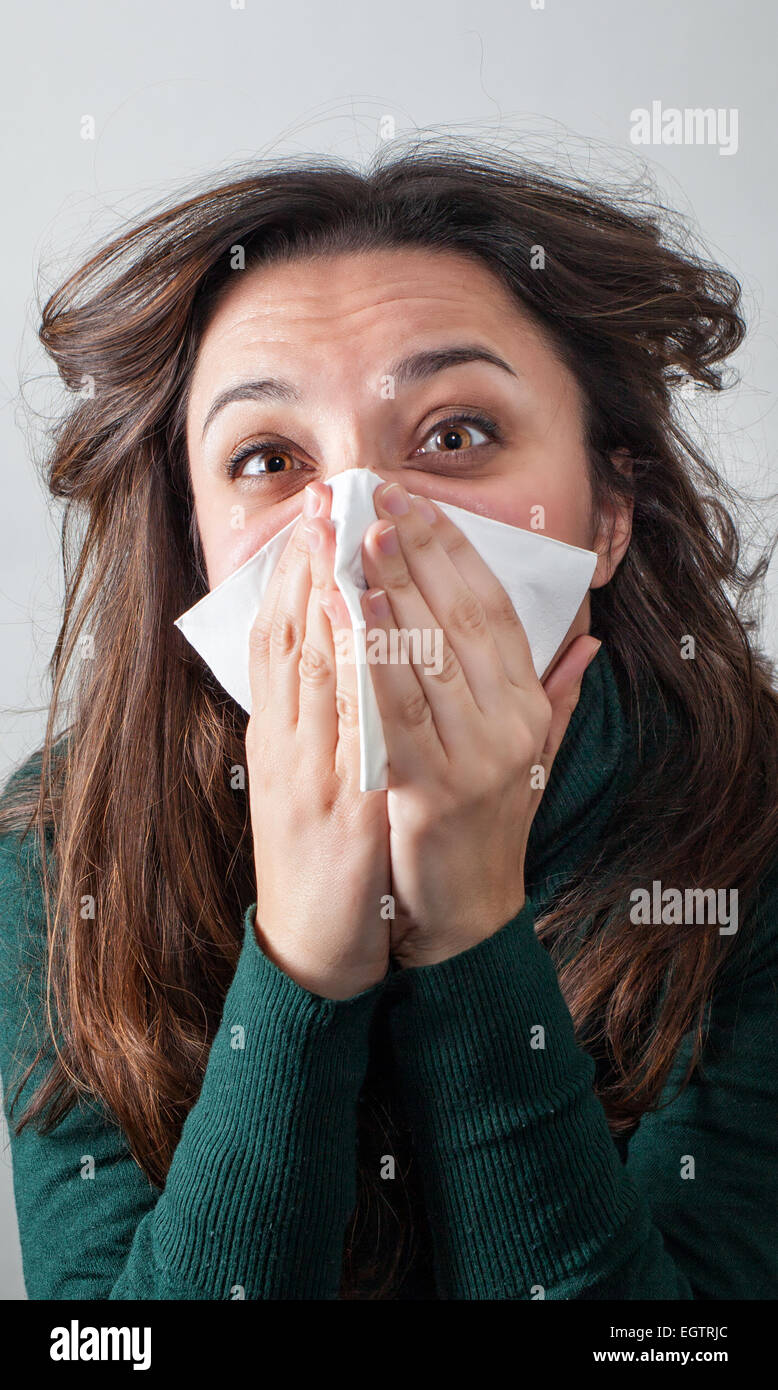 Giovane donna soffia il naso con il fazzoletto di carta su sfondo grigio. Foto Stock