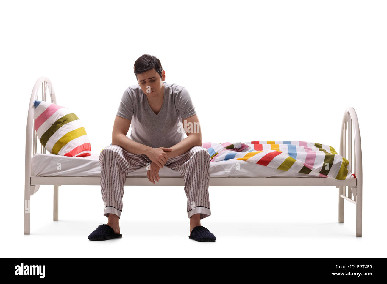 Triste uomo in pigiama seduto su un letto isolato su sfondo bianco Foto Stock