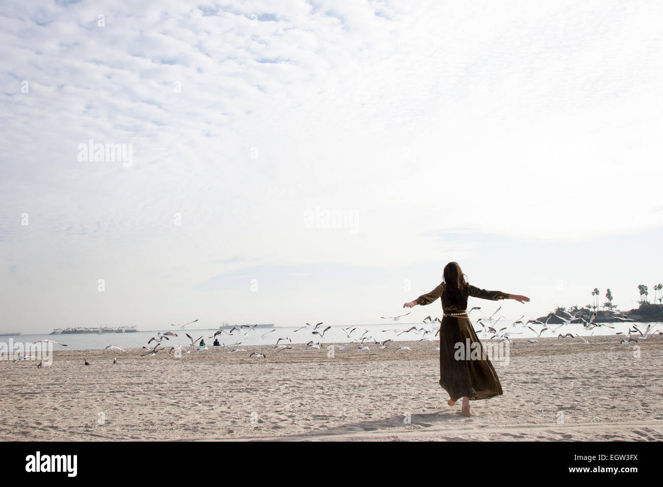 Le donne in scuro abito lungo cammino verso gli uccelli sulla spiaggia. Foto Stock