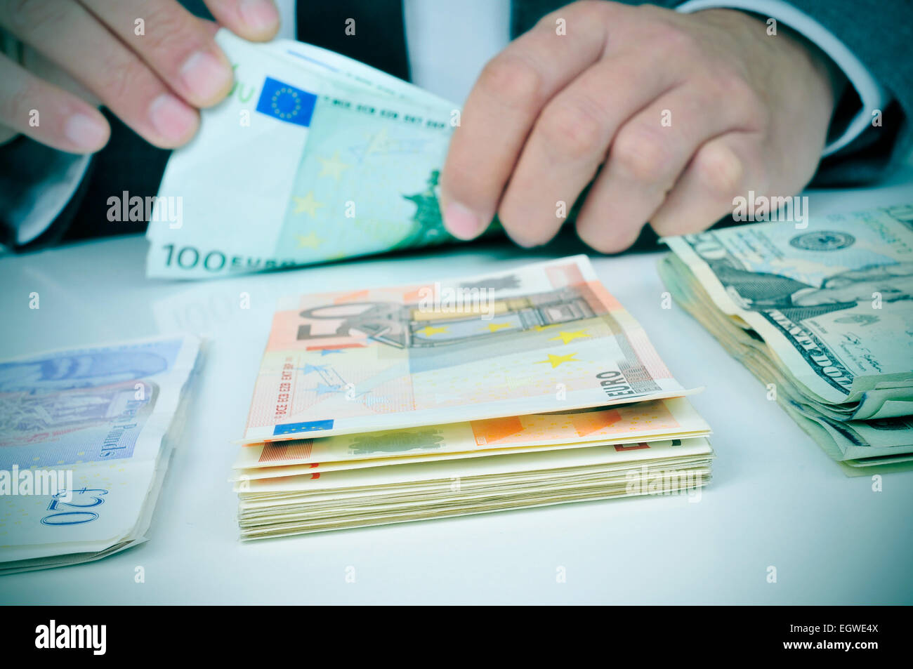 Primo piano delle mani di un giovane uomo che è il conteggio delle banconote in euro su un tavolo con qualche pila di sterlina, euro e dollaro banconote Foto Stock