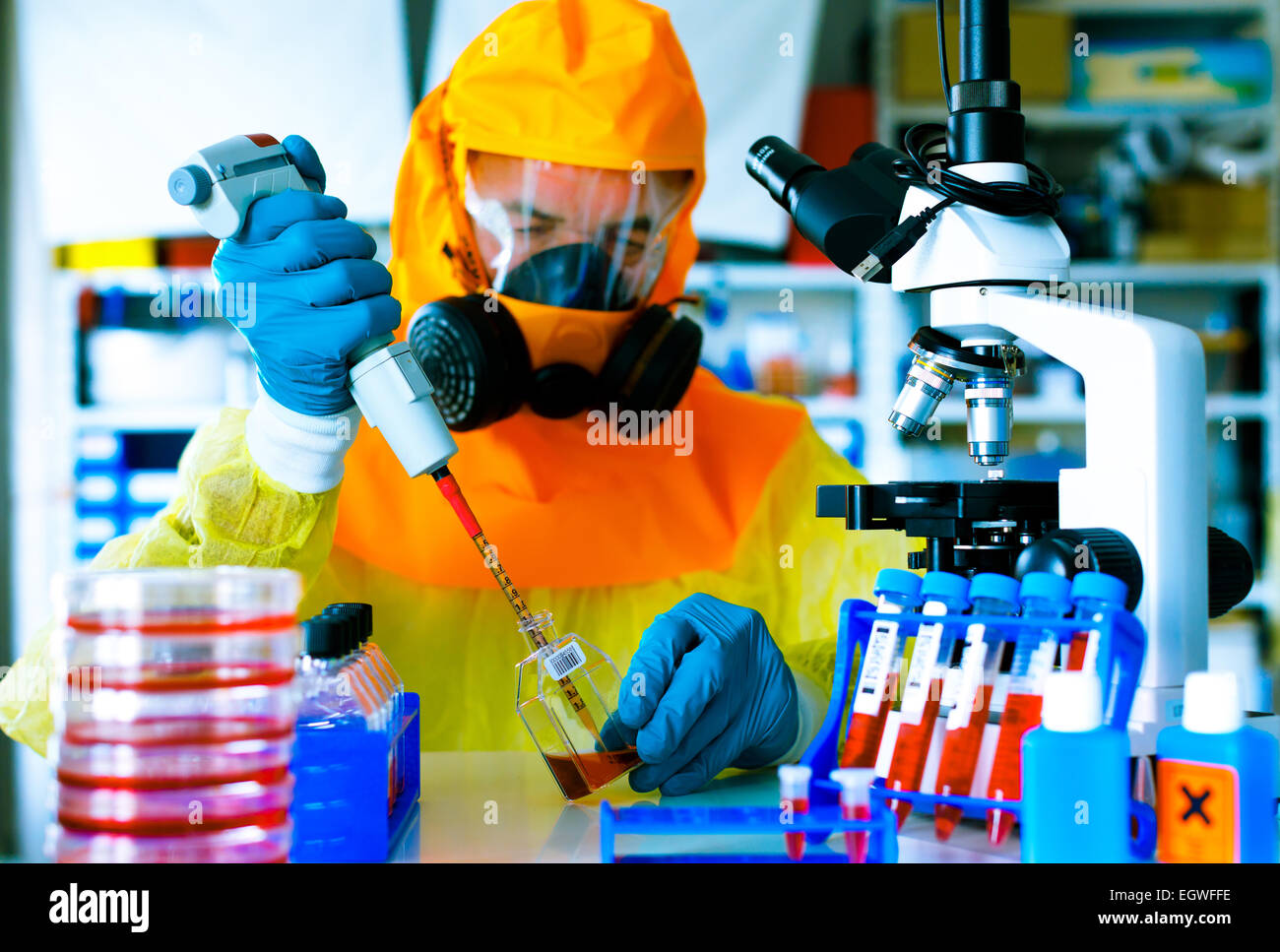 Il test di un vaccino contro il virus Ebola infezione, uno scienziato in tuta protettiva con una pipetta e un microscopio in un laboratorio Foto Stock