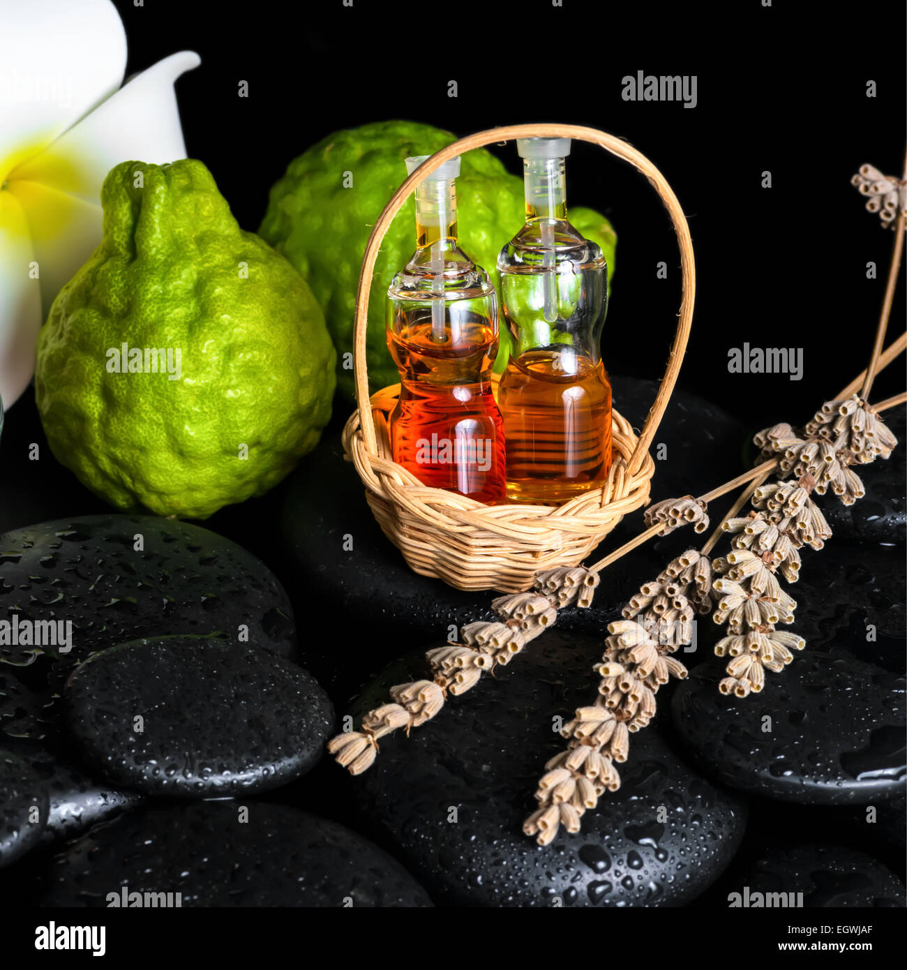 Centro termale aromatico nozione di bottiglie di olio essenziale di bergamotto, frutti, plumeria di fiori e di piante di lavanda essiccata su pietre zen Foto Stock