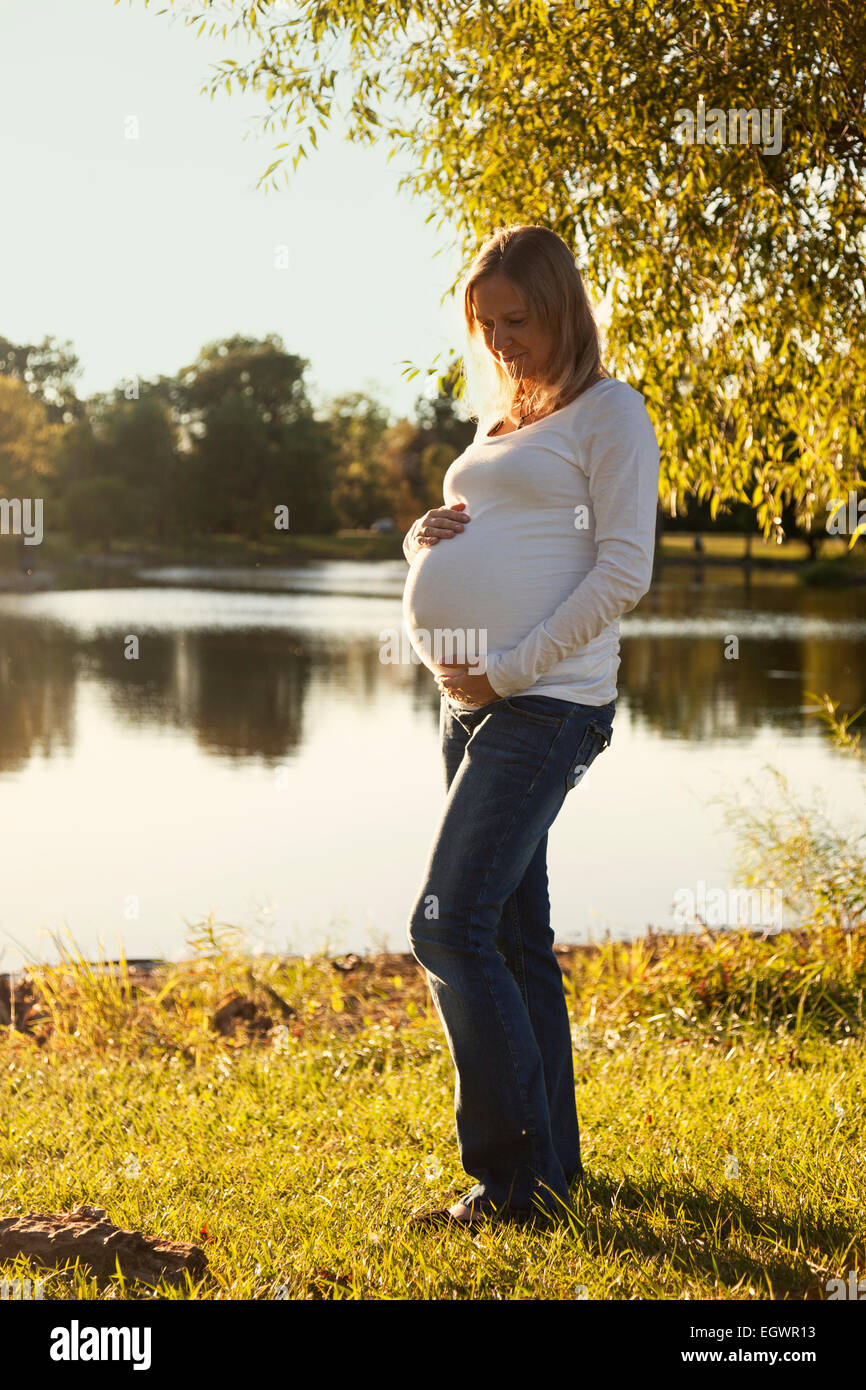 Donna incinta che guarda la sua pancia in un parco al tramonto Foto Stock