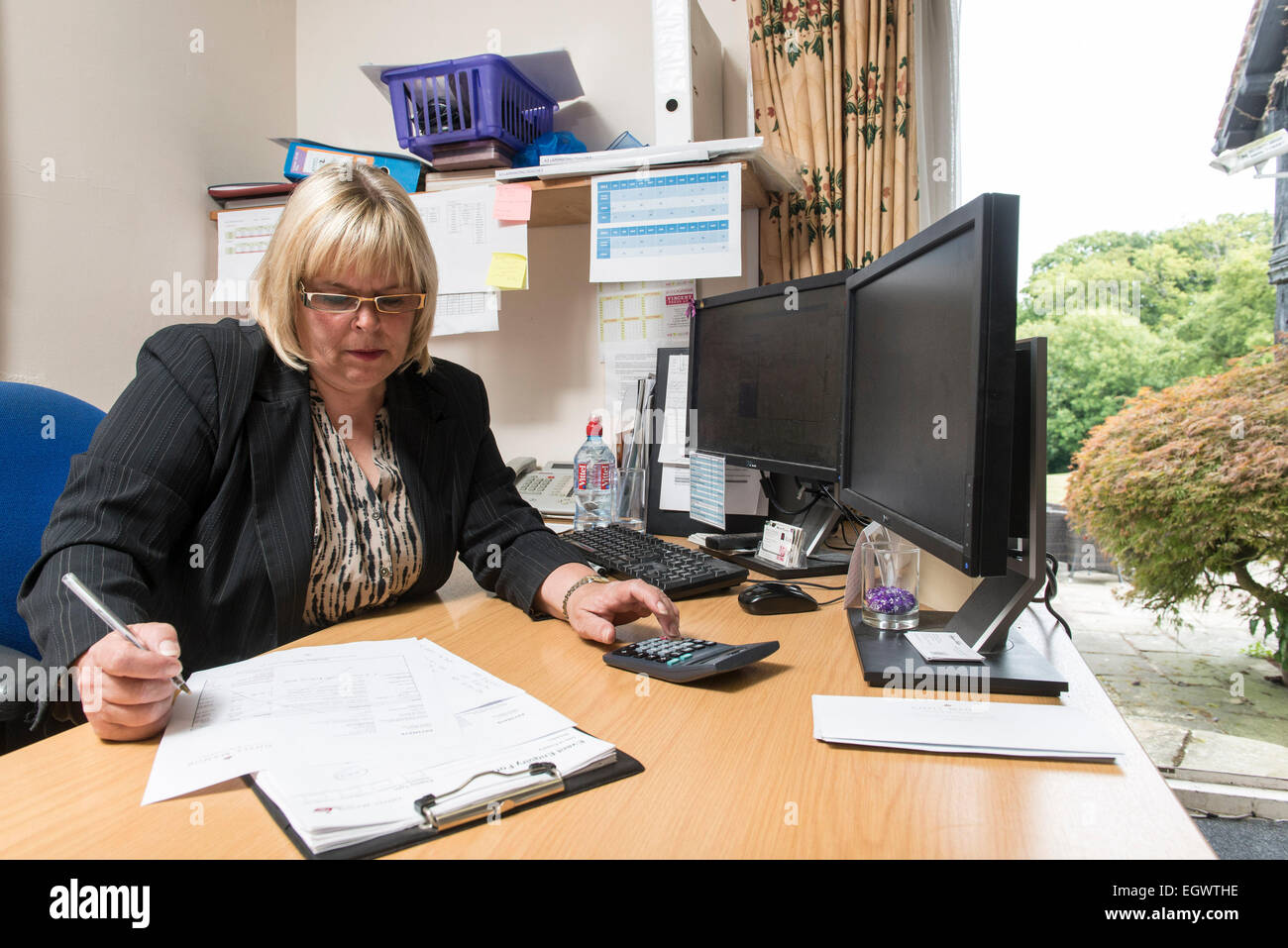 Un amministratore di business office manager dalla sua scrivania in un ambiente di ufficio impegnato la gestione dei diversi aspetti di un hotel e di un lavoro di pianificazione Foto Stock