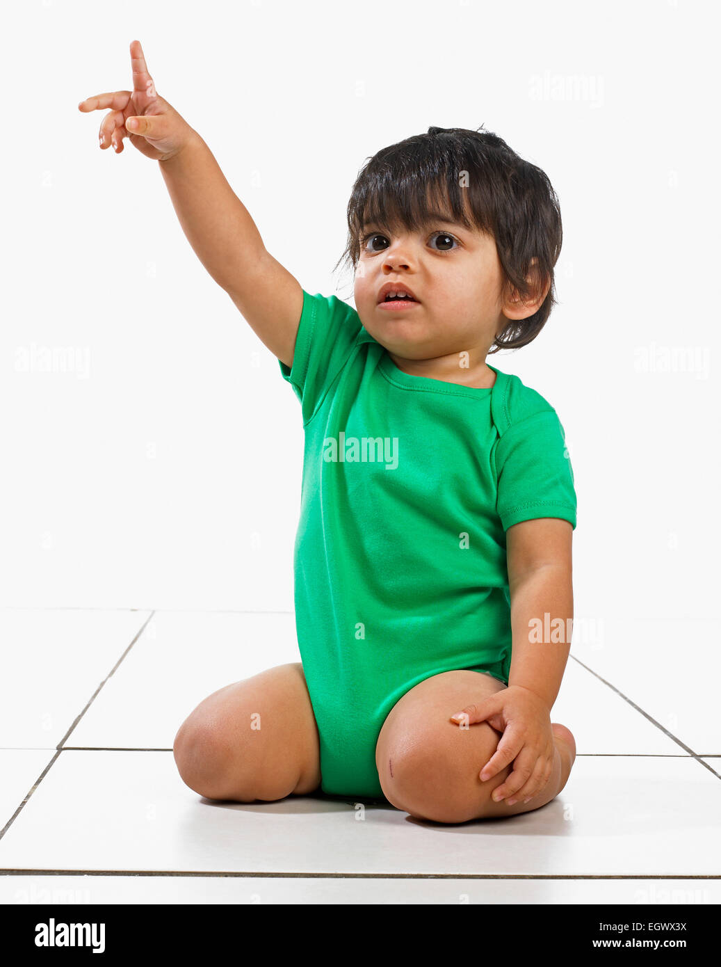 Baby boy (16 mesi) inginocchiati sul pavimento e puntando il dito Foto Stock
