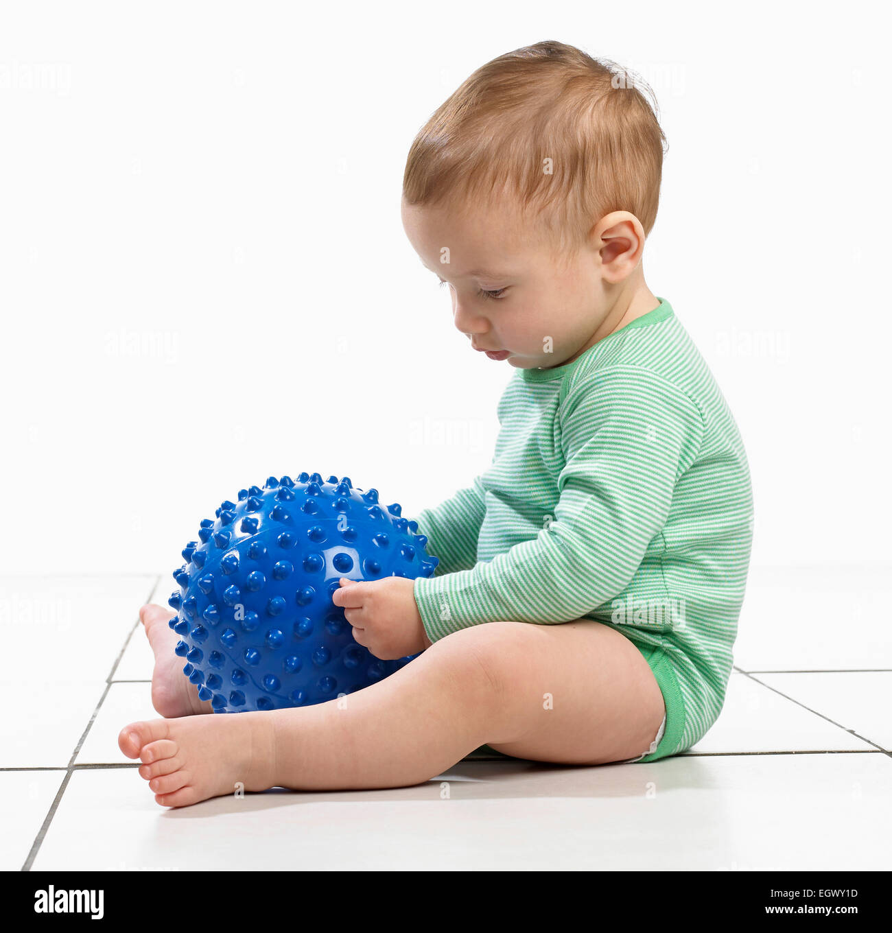 Baby boy (12,5 mesi) seduta tenendo un accidentato giocattolo a sfera Foto Stock