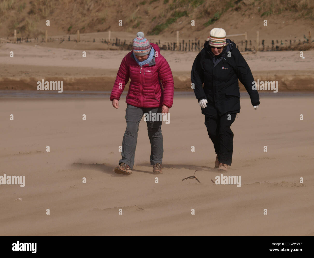 Due donne che lottano per camminare nella direzione del vento su una molto ventoso beach, Woolacombe, Devon, Regno Unito Foto Stock