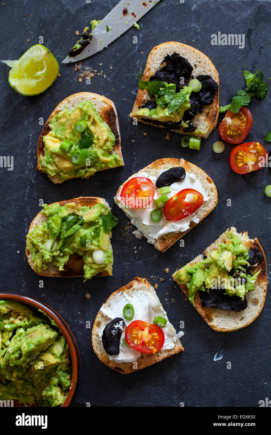 Crostini con diffusione di avocado, formaggio di capra e aglio nero Foto Stock