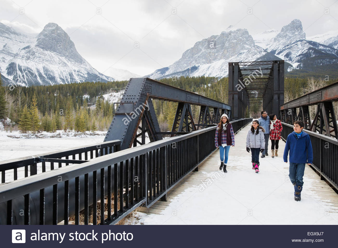 Famiglia camminando lungo il ponte sotto le montagne nevose Foto Stock
