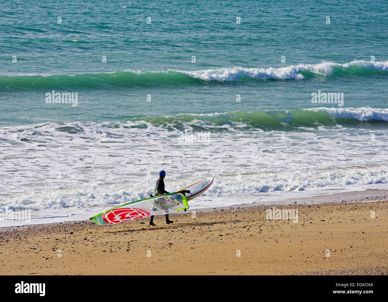 Giovane uomo che porta windsurf in spiaggia, Cornwall, England Regno Unito Foto Stock