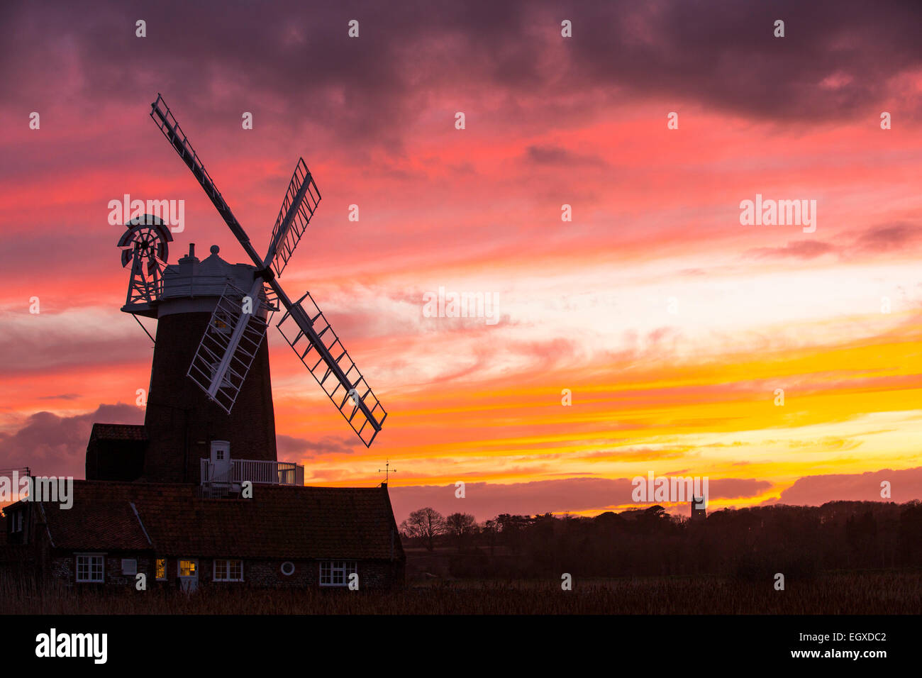 Un mulino a vento a Cley accanto al mare, North Norfolk, Regno Unito, con Blakeney chiesa in background al tramonto. Foto Stock