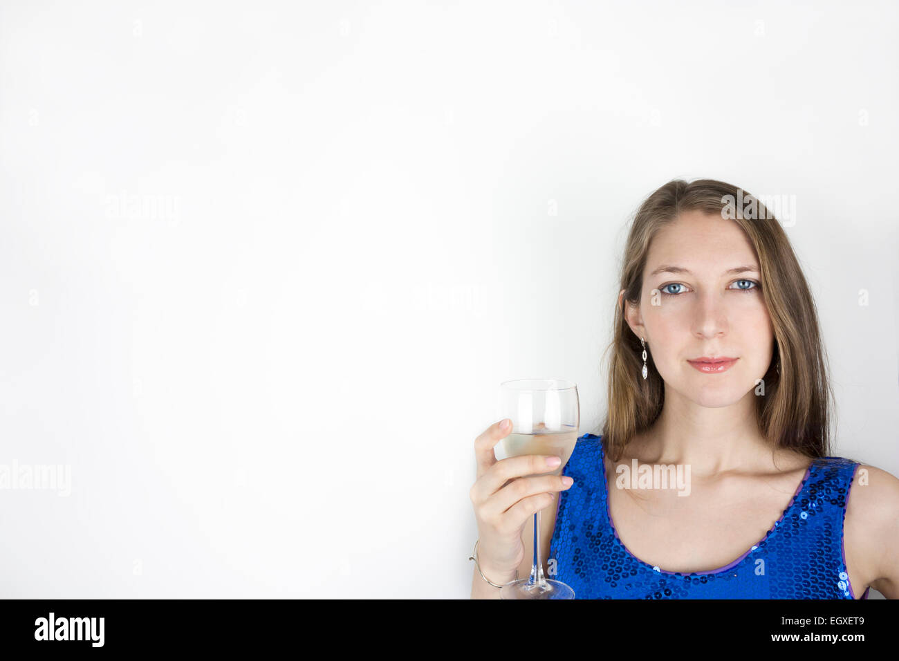 Piuttosto giovane donna che indossa blu abito di paillette e tenendo un bicchiere di vino bianco Foto Stock