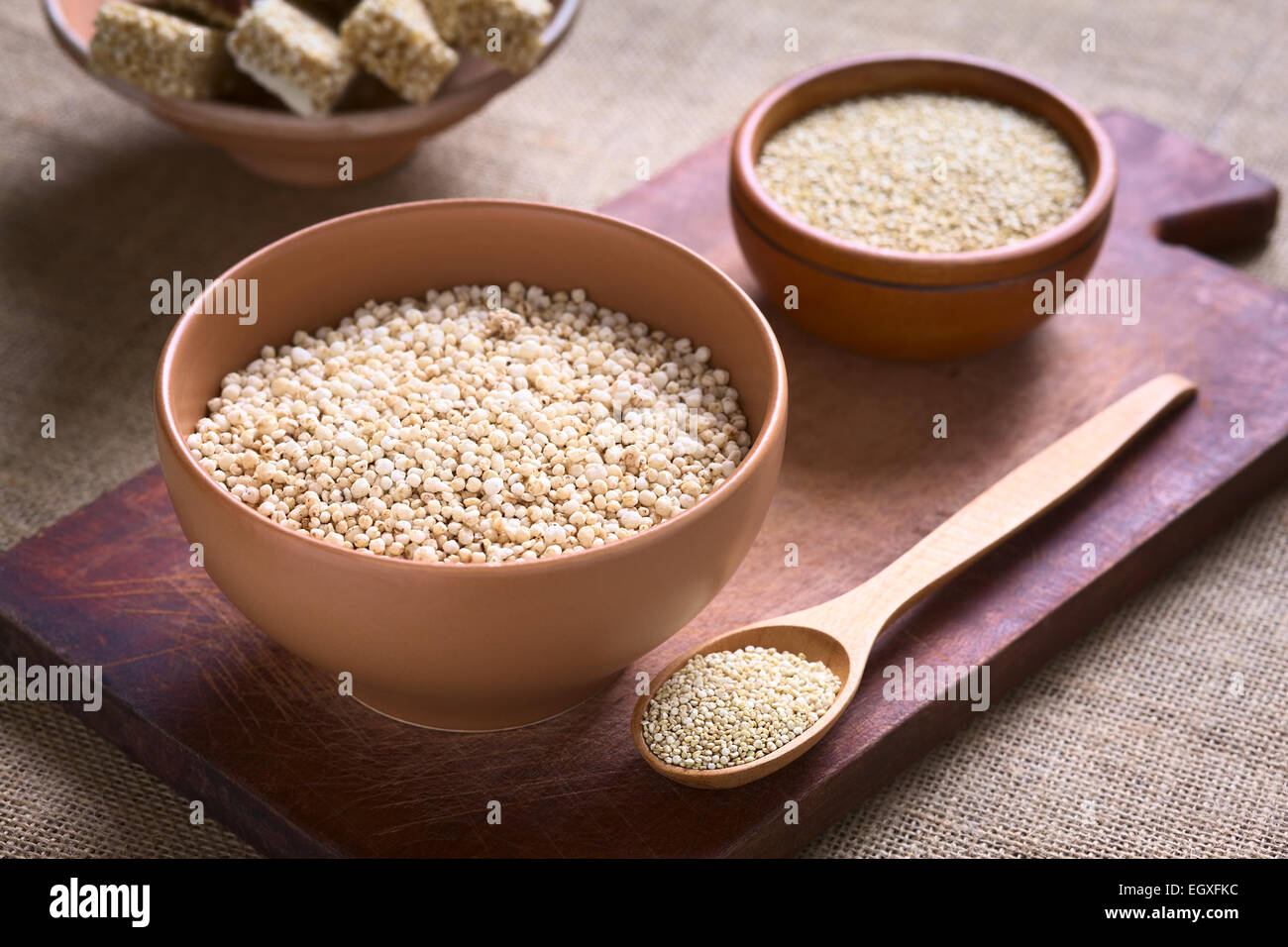 Popping quinoa bianco (lat. Chenopodium quinoa) il cereale nella ciotola con materie di quinoa le sementi e la quinoa barrette di cereali nella parte posteriore Foto Stock