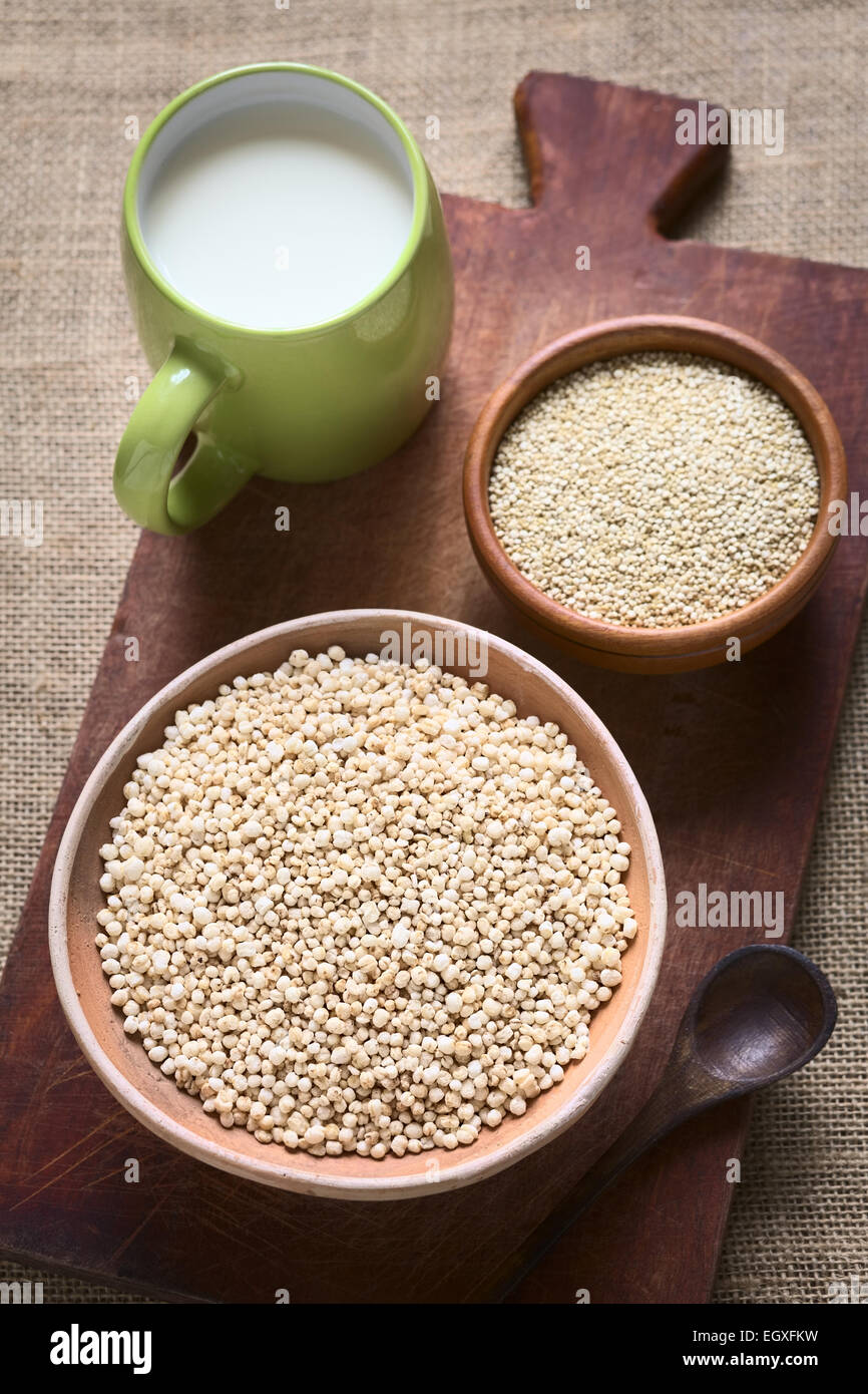 Popping quinoa bianco (lat. Chenopodium quinoa) il cereale nella ciotola con materie di quinoa le sementi e la tazza di latte nel retro Foto Stock