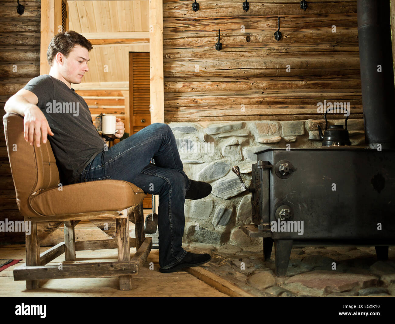 Lonely Man seduto di fronte a una combustione lenta stufa e rilassante con pantofole e tazza di caffè. Foto Stock