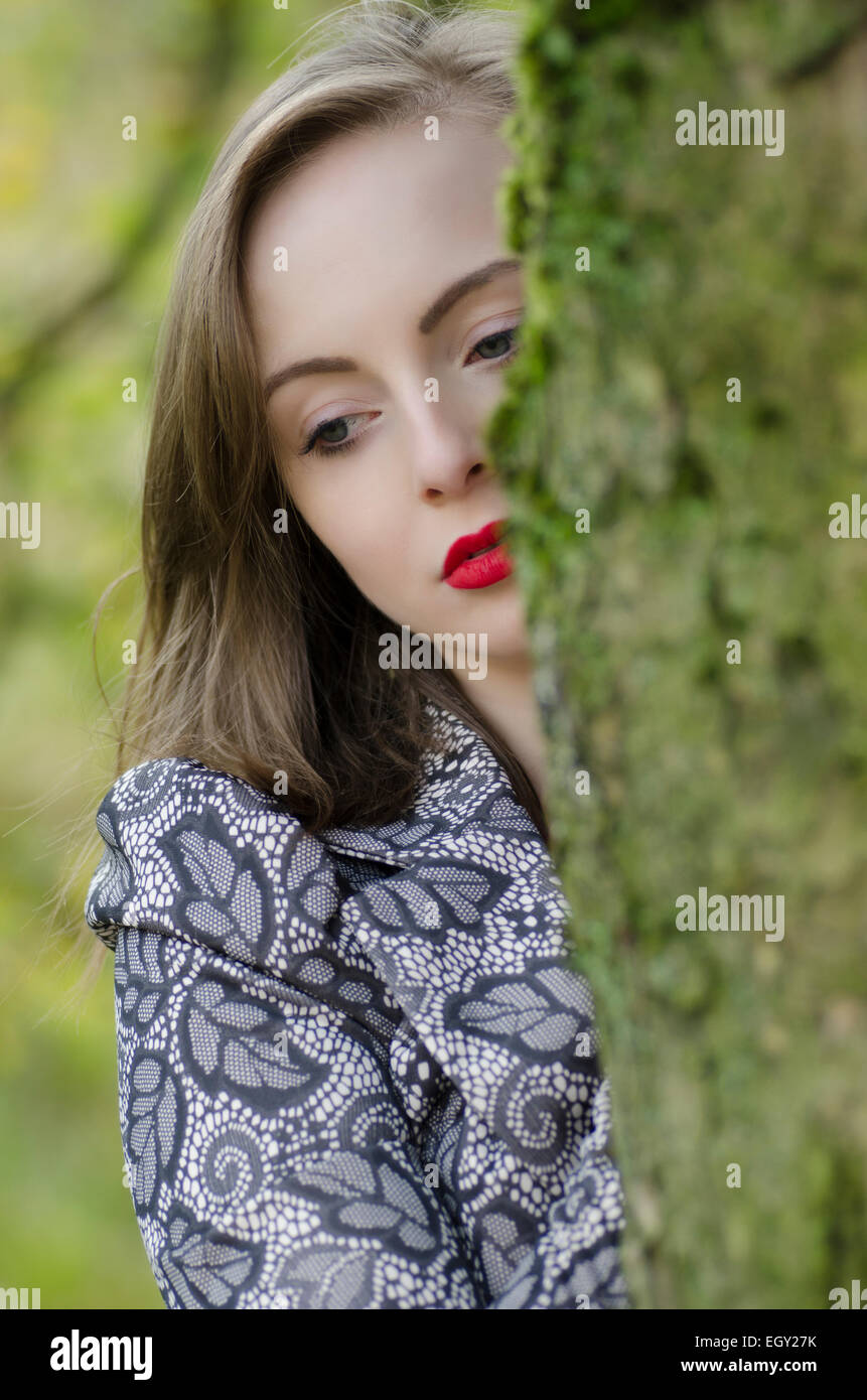 Considerato giovane donna in piedi dietro a un albero Foto Stock