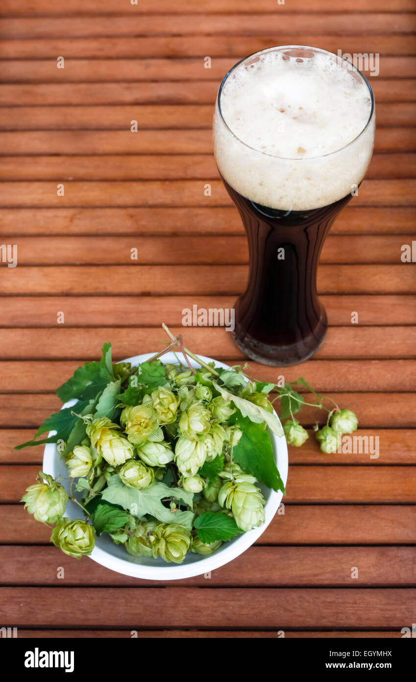 Bicchiere di birra scura e una ciotola di hop su legno Foto Stock