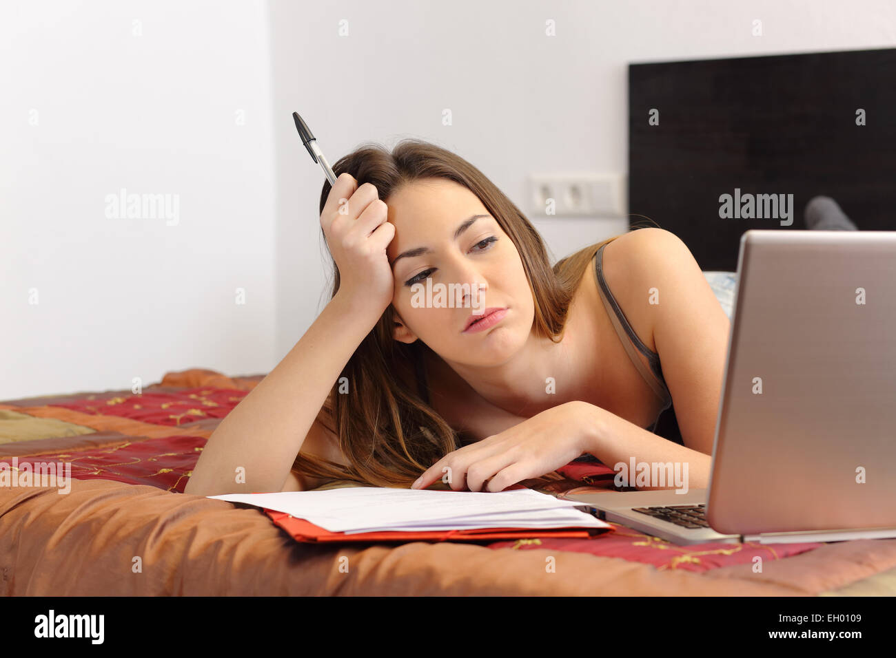 Annoiato studente con un computer portatile in camera da letto a casa Foto Stock