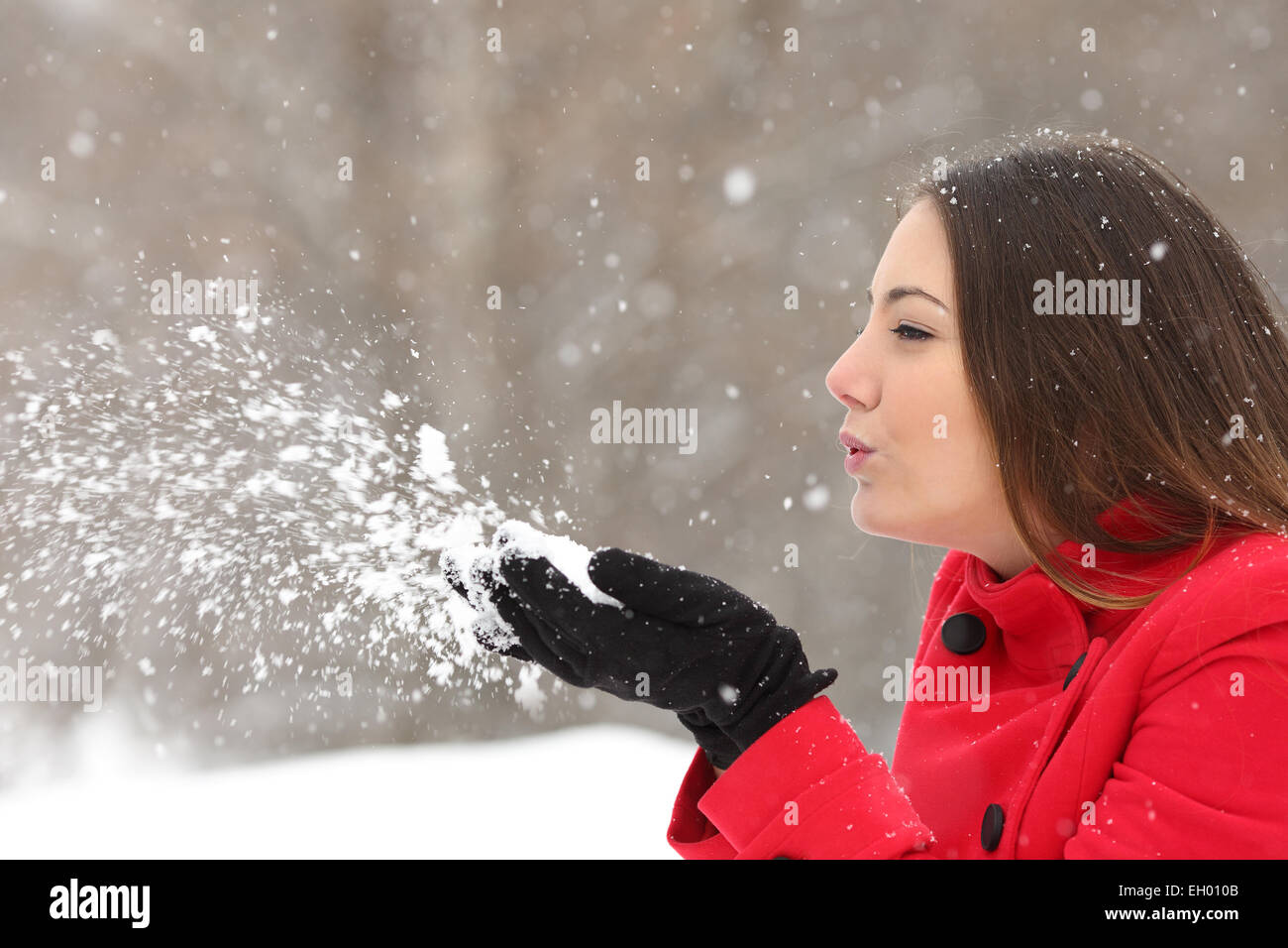 Vista laterale di una candida woman in red soffiando la neve in inverno durante una nevicata Foto Stock