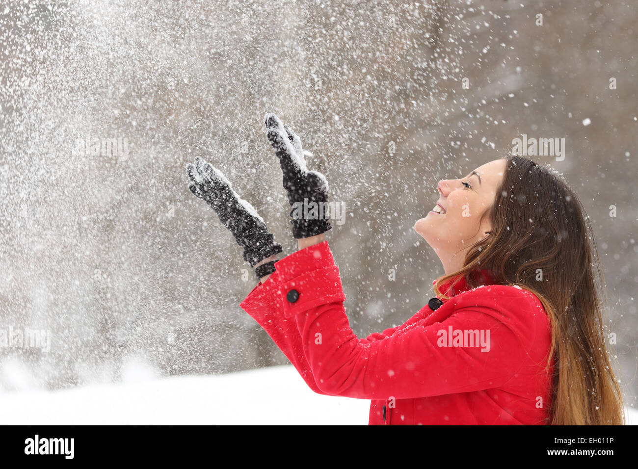 Donna che indossa una giacca rossa gettando la neve in aria in vacanze invernali Foto Stock