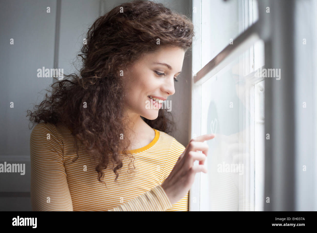 Sorridente giovane donna cuore di pittura su vetro di finestra Foto Stock