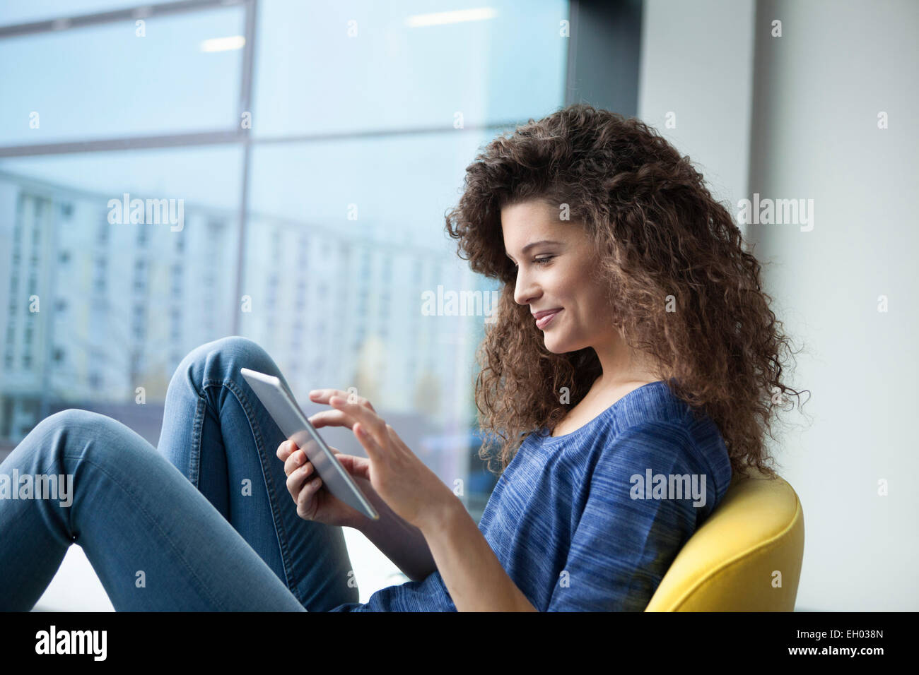 Sorridente giovane donna con tavoletta digitale in corrispondenza della finestra Foto Stock