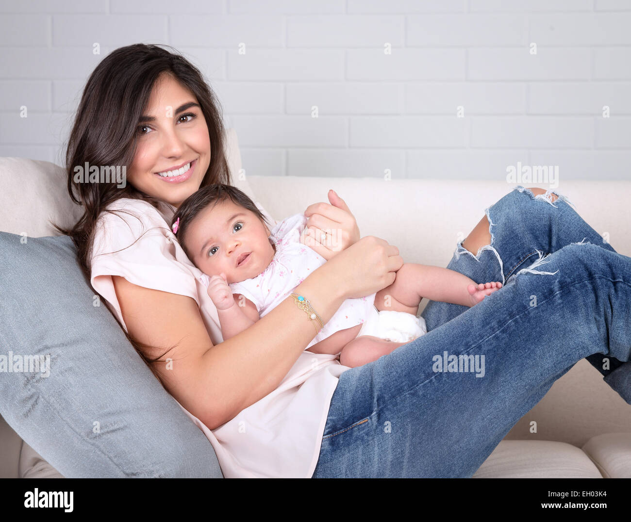 Allegro giovane madre comodamente seduti sul divano di casa e giocare con il piccolo grazioso baby, felice della maternità, di amore e di felicità Foto Stock