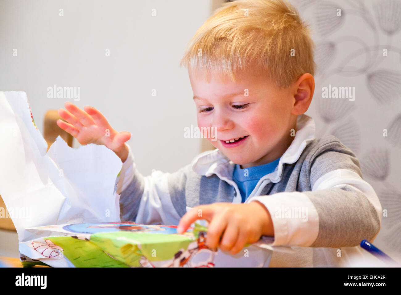 Giovani dai capelli biondi caucasian boy eccitato apre regalo di compleanno nel Regno Unito Foto Stock