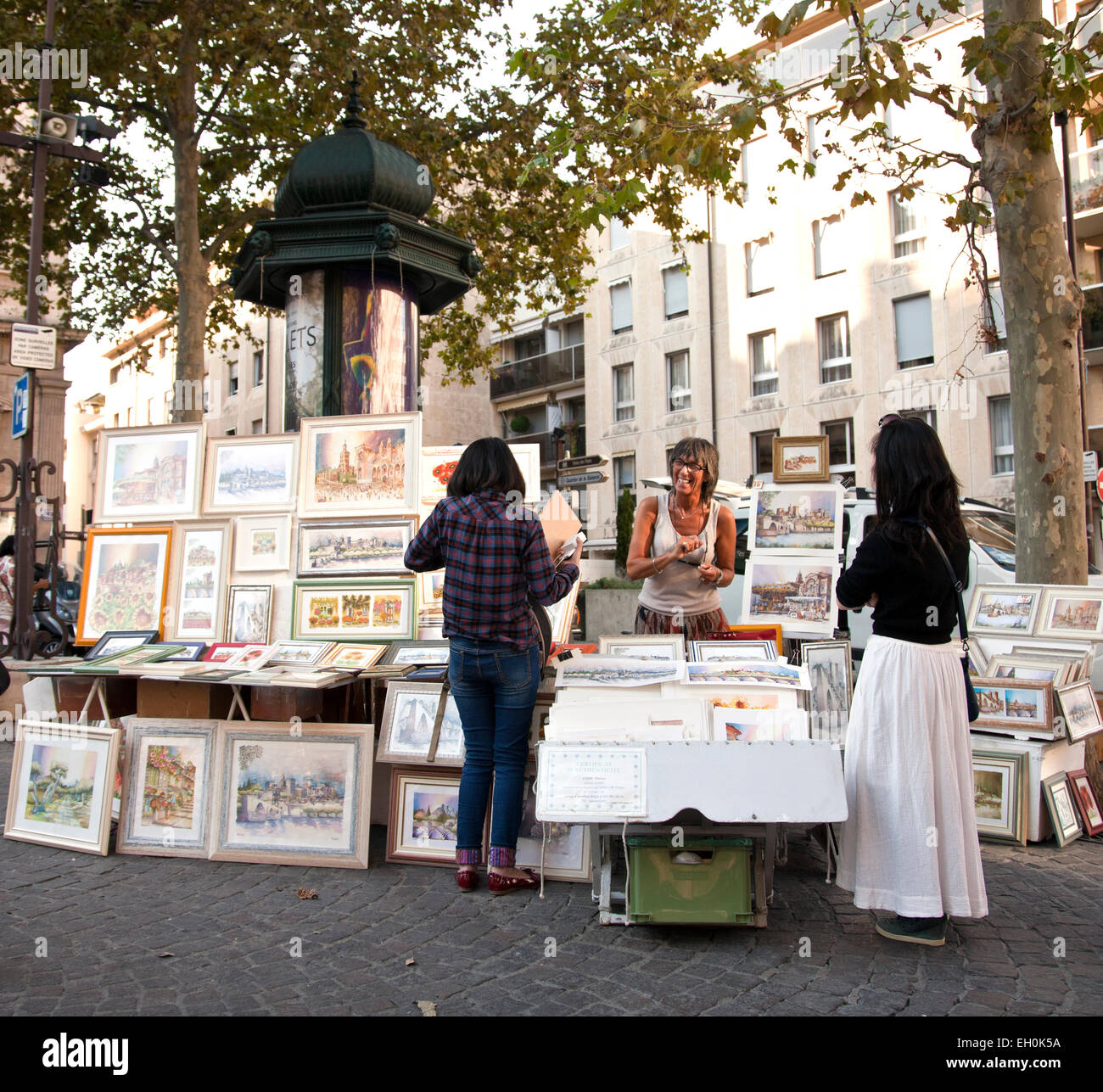 Artista Pascale Cozic accoglie due turisti per la sua arte stand in Place de L'Horloge a Avignon, Francia. Foto Stock