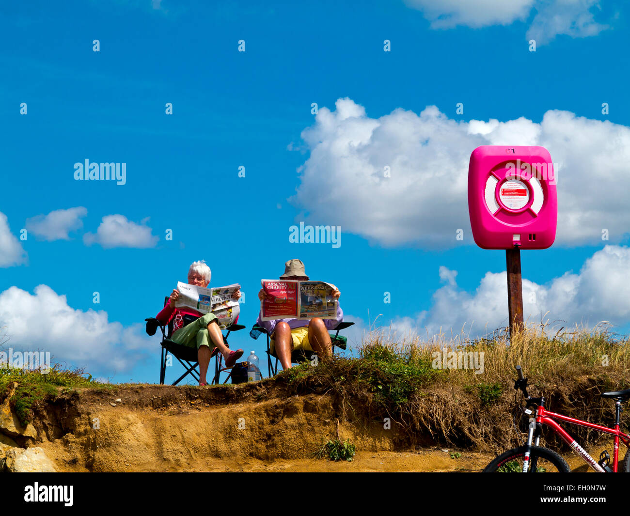 Coppia di anziani seduti su sedie a sdraio la lettura sulla spiaggia di Burton Bradstock nel Dorset sulla costa sud-ovest dell'Inghilterra, Regno Unito Foto Stock
