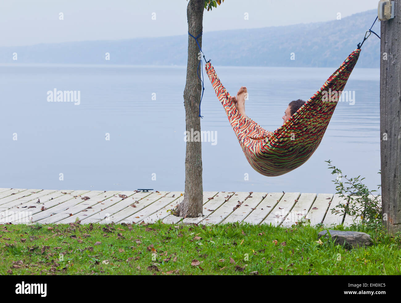 L uomo si rilassa in amaca sulla riva del lago. Foto Stock