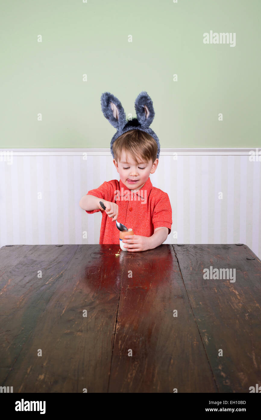 Carino piccolo ragazzo con orecchie di coniglietto di mangiare un uovo sodo. Foto Stock