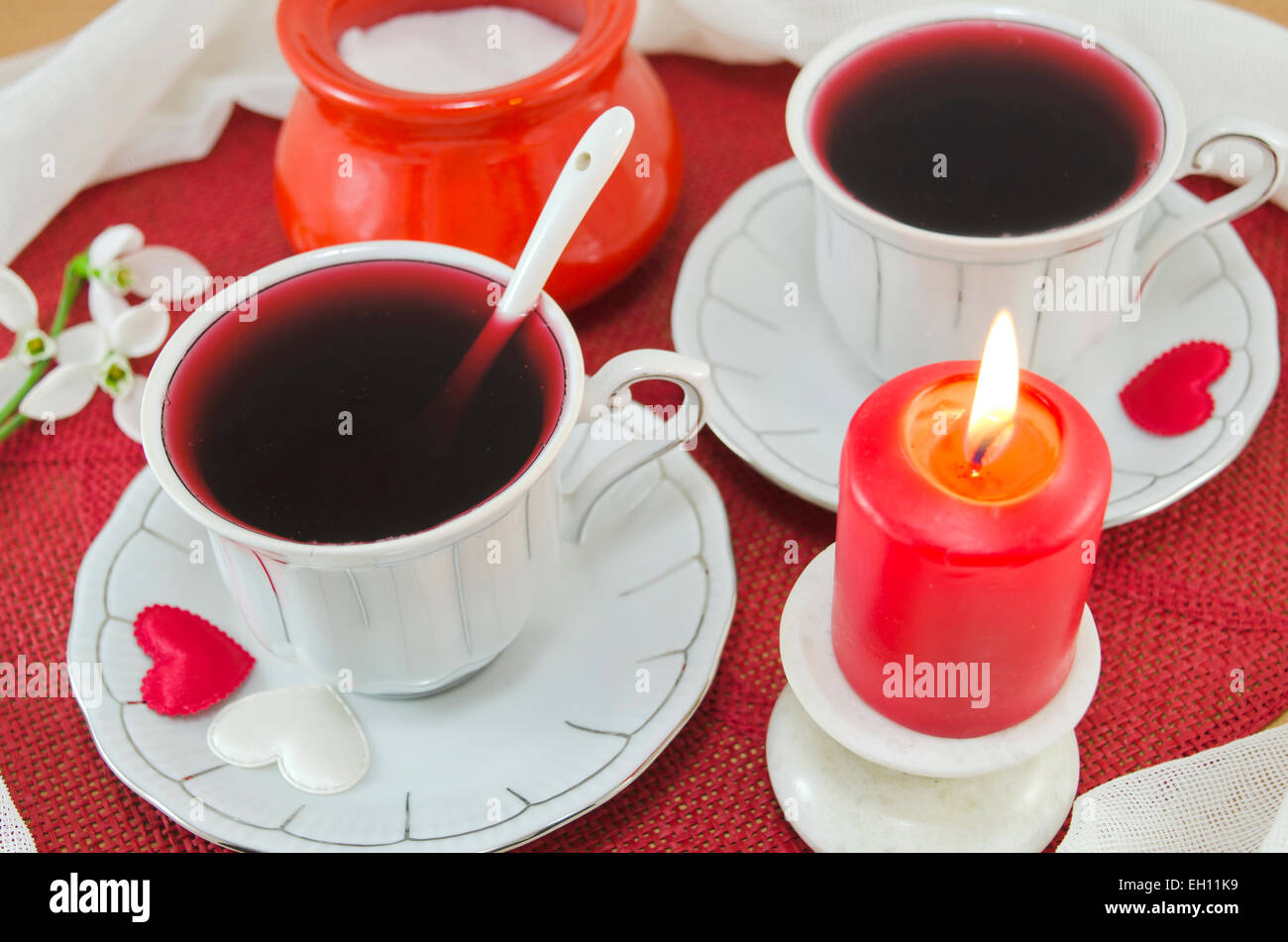 Due tazze di tè di ibisco decorata con due cuori e una candela che brucia Foto Stock